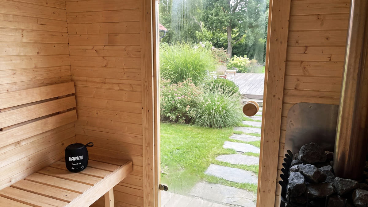 Timber bench inside an outdoor sauna, with the garden seen through the glass door