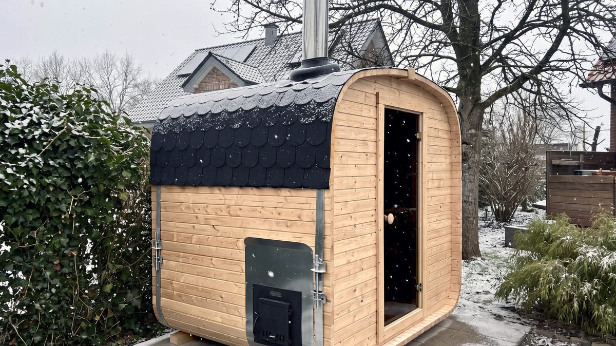 Wood-fired outdoor sauna with its flue and side firebox hatch in a snowy garden