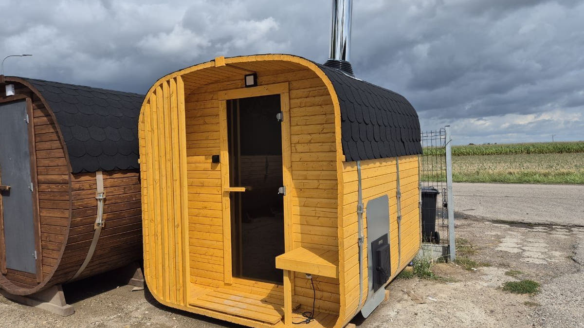 A barrel sauna and a cube-shaped outdoor sauna side by side, the cube with a stainless flue