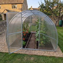 SteelRoot Plot 3.14 greenhouse in a stone cottage garden, door open, tomatoes and cucumbers inside