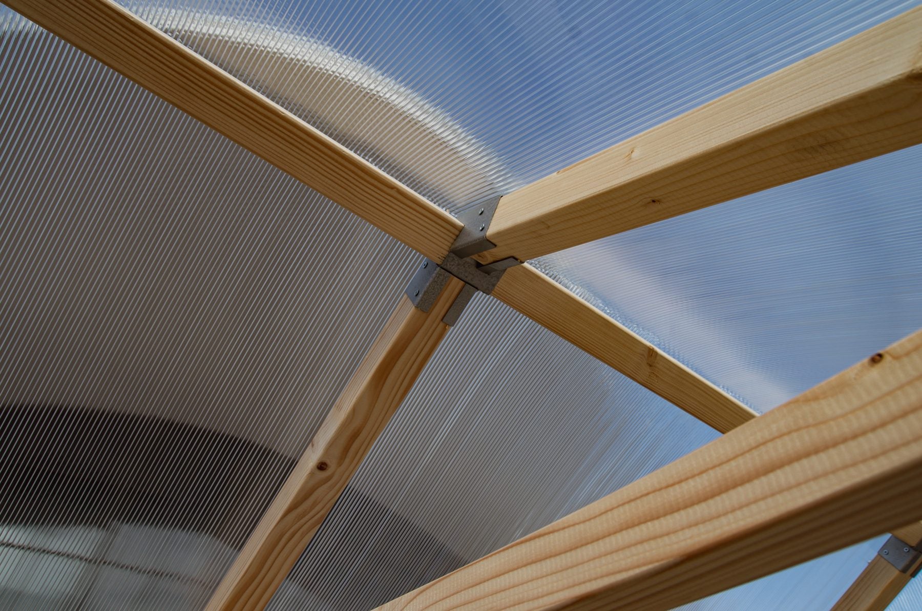 Twin-wall polycarbonate roof and pine rafters of a NORDIC greenhouse, seen from below