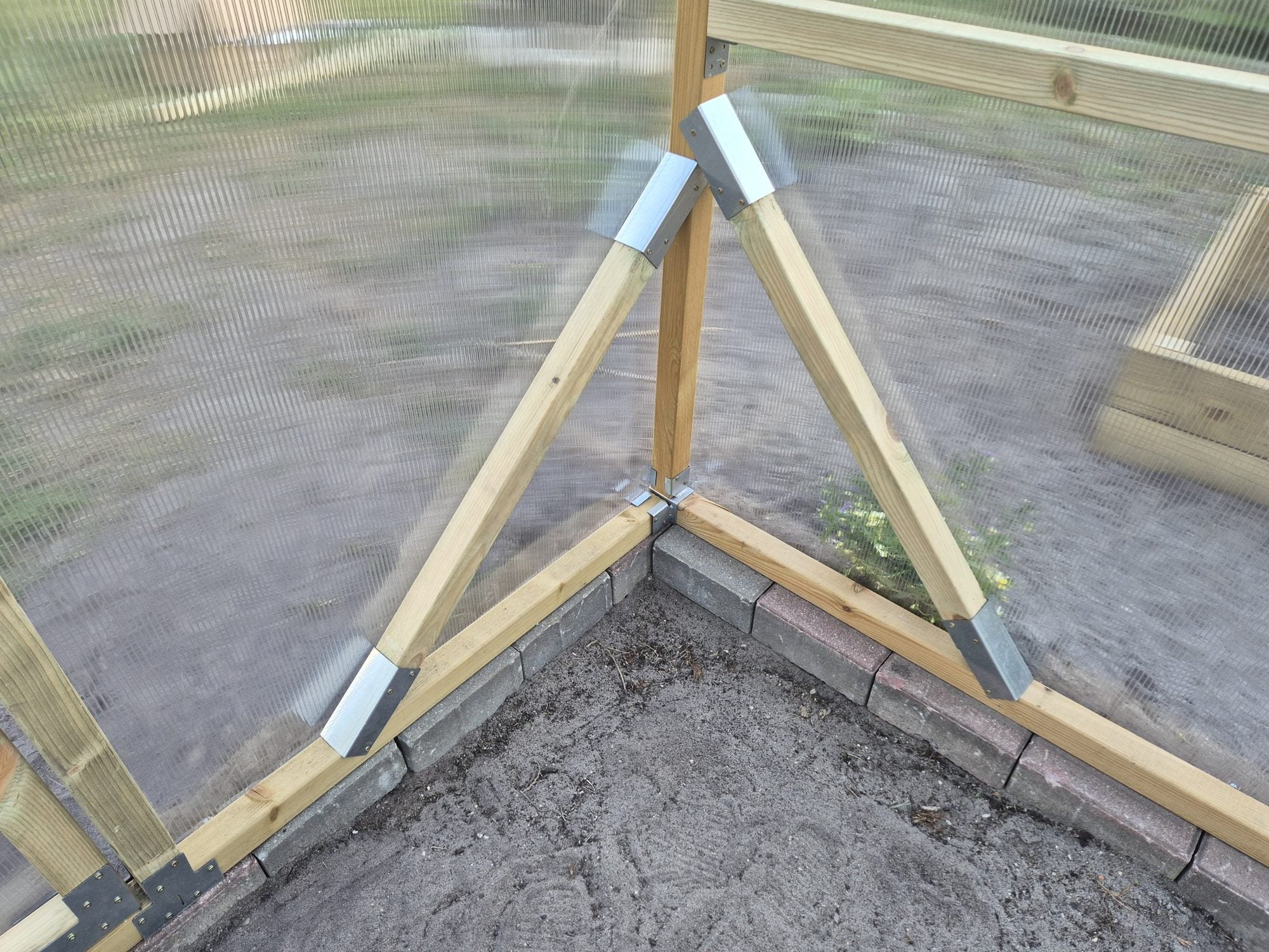 Diagonal corner braces and galvanised brackets at the base of a NORDIC wooden greenhouse