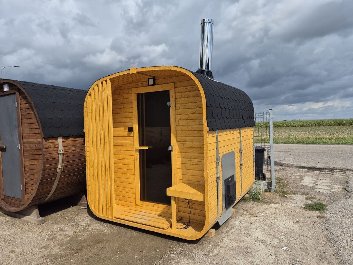 A barrel sauna and a cube-shaped outdoor sauna side by side, the cube with a stainless flue