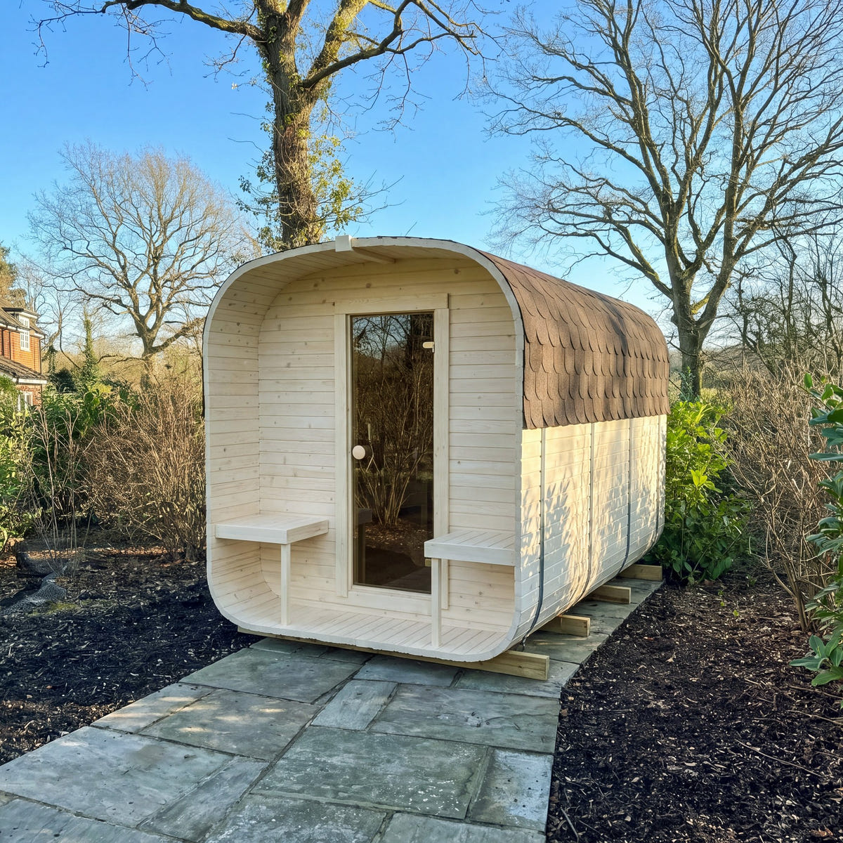The Cabin Six Two-Tier electric sauna on a paved garden path, in a pale finish, with its glass door and porch seats