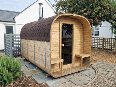 The Cabin Six Two-Tier outdoor sauna on a paved corner beside a white cottage