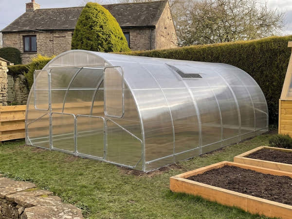 SteelRoot Grand 4.00 arch greenhouse by a stone cottage, with raised beds in front